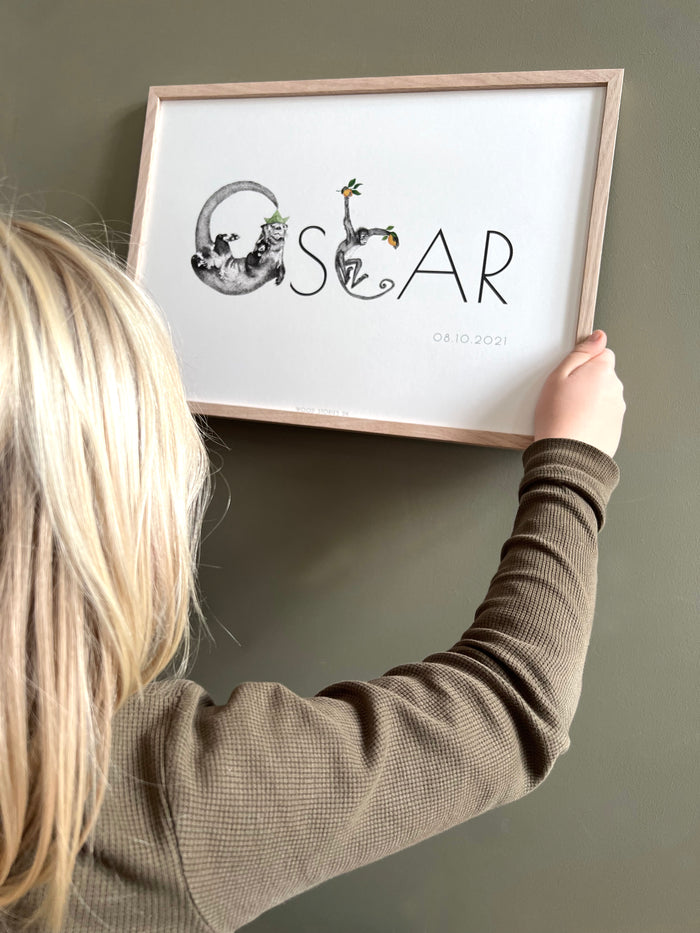Dreng hænger navneplakat, med navnet Oscar, med dyr og bogstaver op på væggen